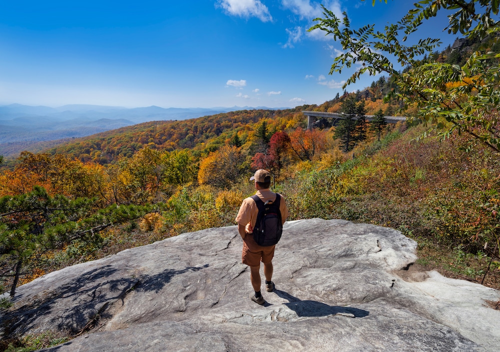 Man standing at the top of a hike taking in the view of Blue Ridge Parkway fall colors near our Shenandoah Valley c